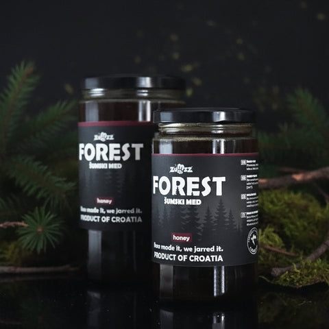 Two jars of 'Forest' honey with a dark background and greenery.